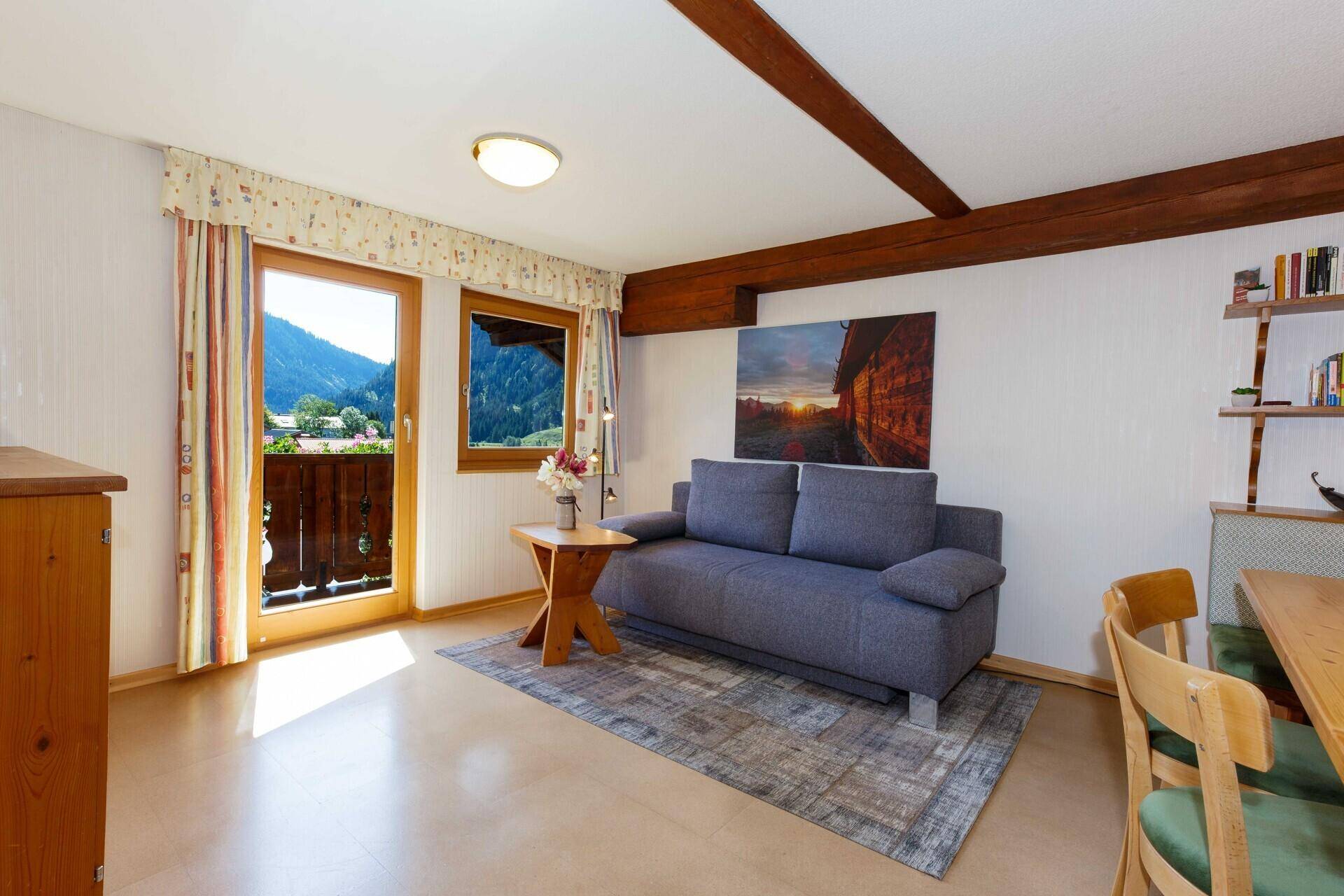 Heller Wohn-Essbereich mit Sofa, Esstisch und Balkonzugang mit Bergblick.