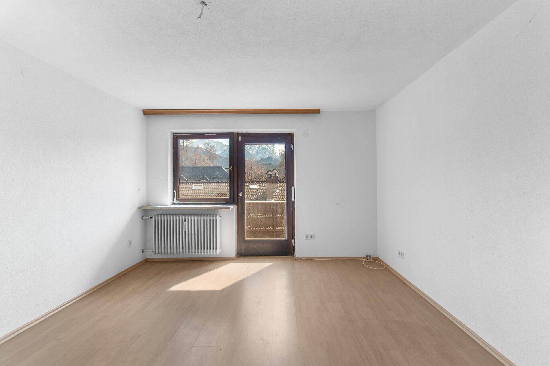 Heller Wohnraum mit Laminatboden, Balkonzugang und Bergblick.