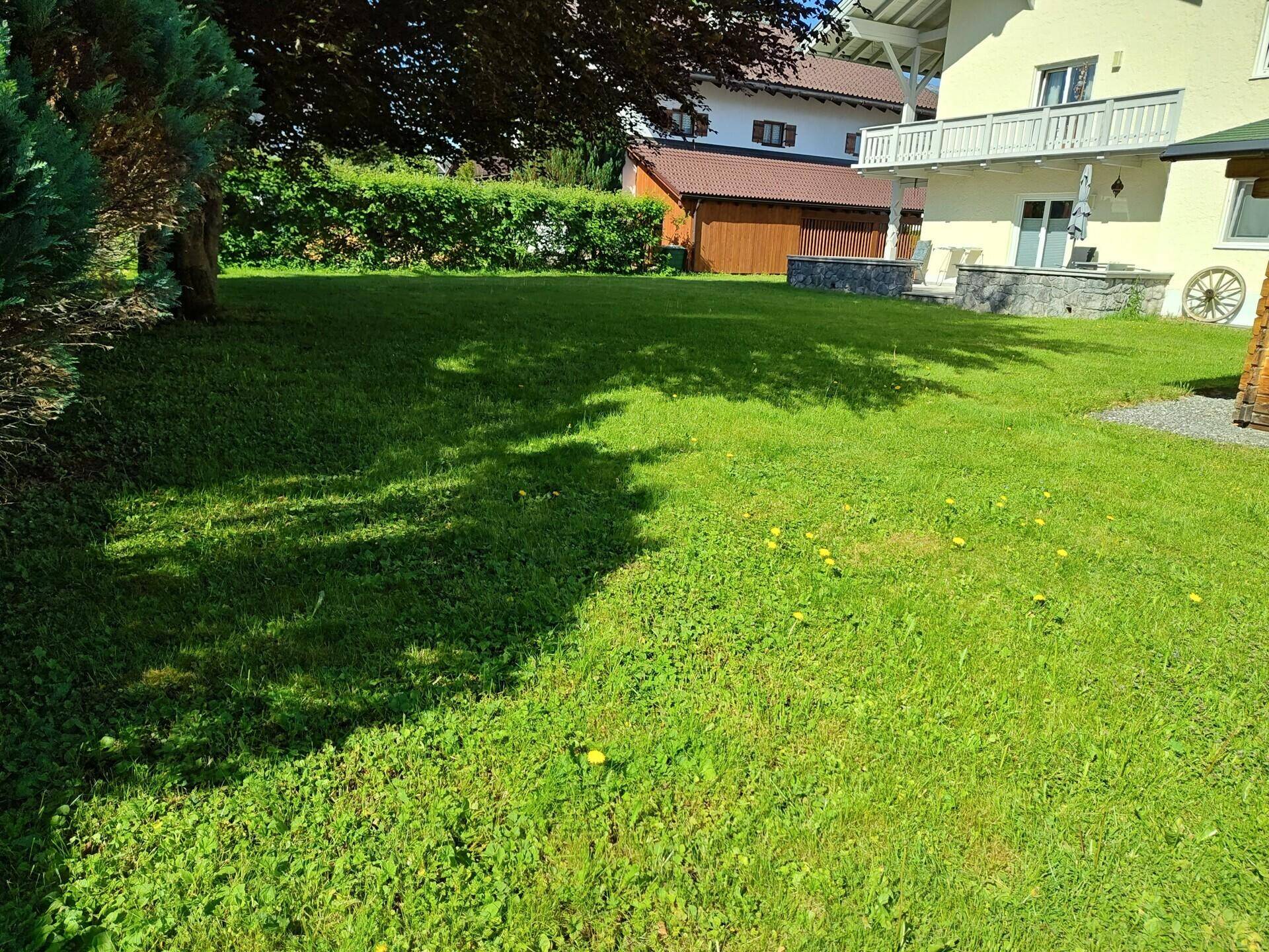 Großer, gepflegter Garten mit Rasenfläche und einem Haus mit Balkon im Hintergrund.
