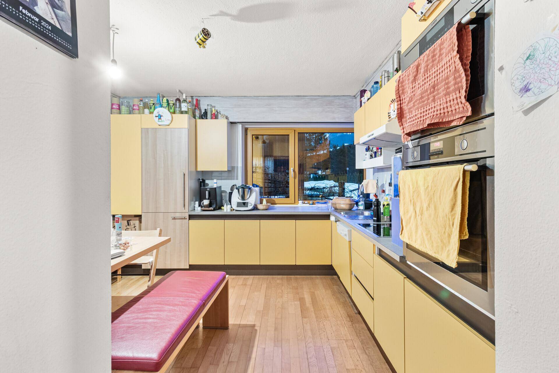 Moderne Küche mit gelben Fronten, Holzboden und integrierten Geräten, ideal für gemeinsame Mahlzeiten.