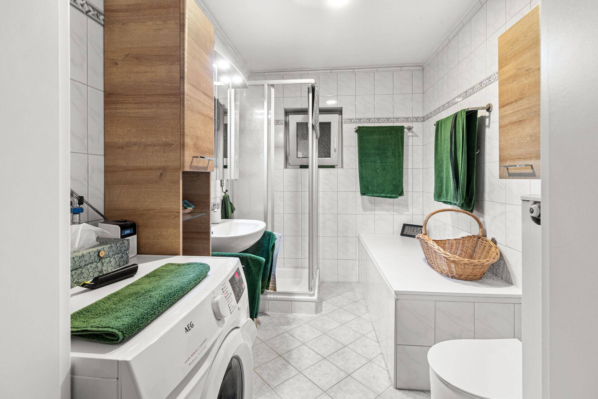 Modernes Badezimmer mit Dusche, Waschmaschine und hellen Fliesen.