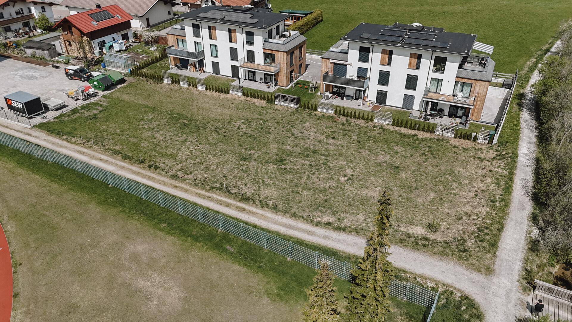 Moderne Wohngebäude mit Balkonen und Terrassen blicken auf ein weitläufiges, grünes Grundstück mit Sportanlage.