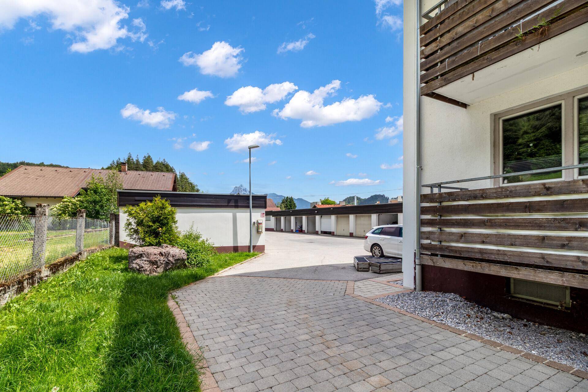 Außenbereich mit gepflasterter Zufahrt, Parkplätzen und Garagen in ländlicher Umgebung.