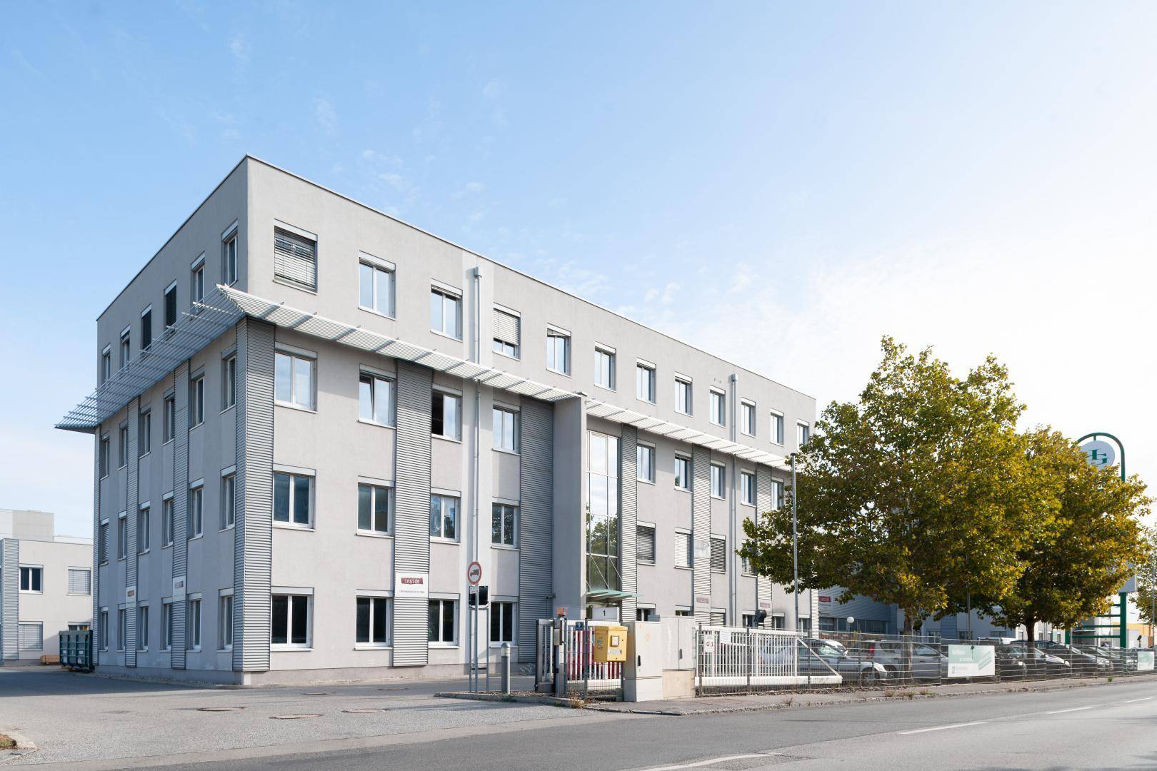 Modernes Bürogebäude mit mehreren Etagen, großen Fenstern, gepflegter Außenanlage und Parkplätzen.