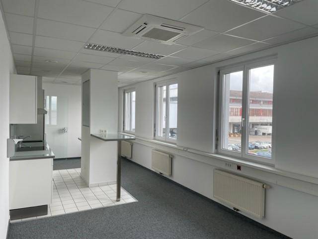 Heller Büroraum mit kleiner Küchenzeile, Teppichboden und Fenstern mit Ausblick.