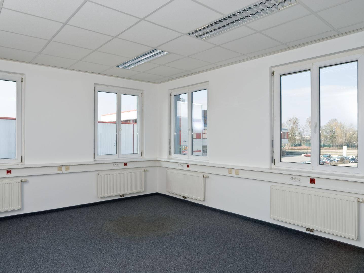 Geräumiges Büro mit Teppichboden, vielen Fenstern und Blick auf die umliegende Bebauung.