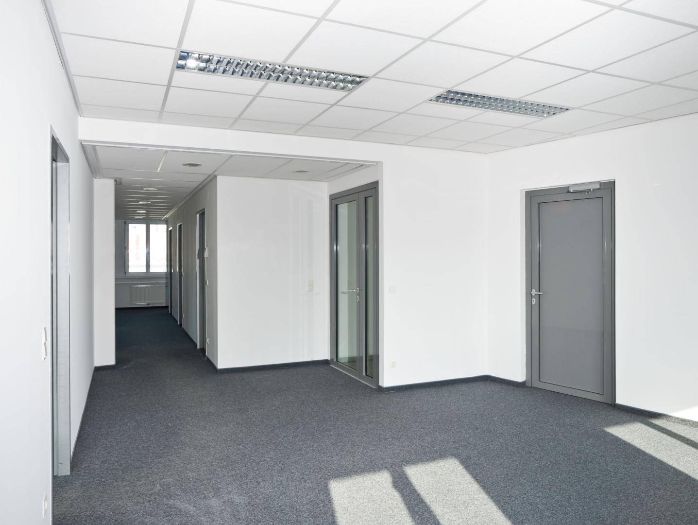 Geräumiger Flur mit Teppichboden und Zugang zu mehreren Büroräumen, hell durch Tageslicht.