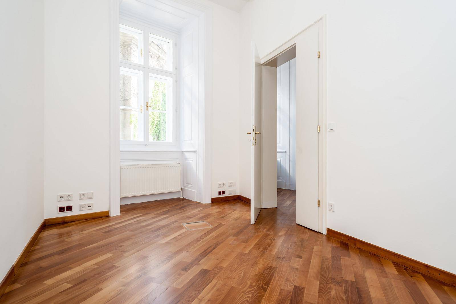 Leerer Raum mit Holzboden und einem großen Fenster, das für viel natürliches Licht sorgt.