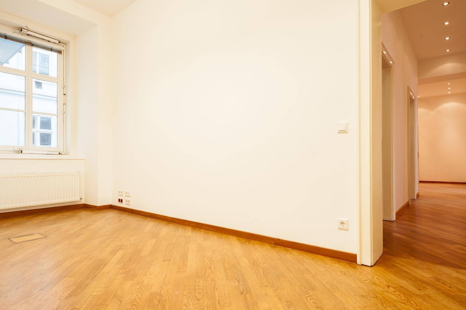 Heller Büroraum mit Holzboden und einem Fenster, das den Blick nach draußen freigibt.