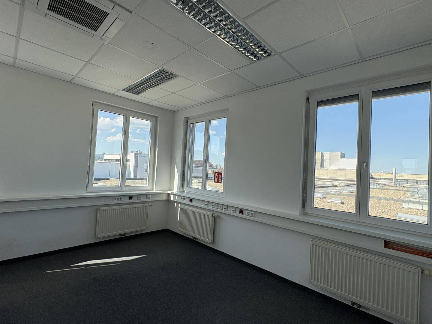 Modernes Büro mit Teppichboden und Fenstern, die einen Blick auf umliegende Gebäude und Dächer ermöglichen.