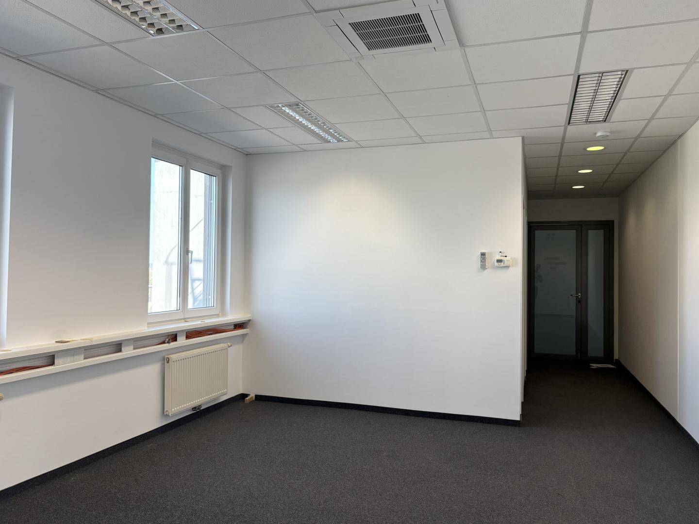 Geräumiges Büro mit Teppichboden und schlichten weißen Wänden, ideal für verschiedene Büronutzungen.