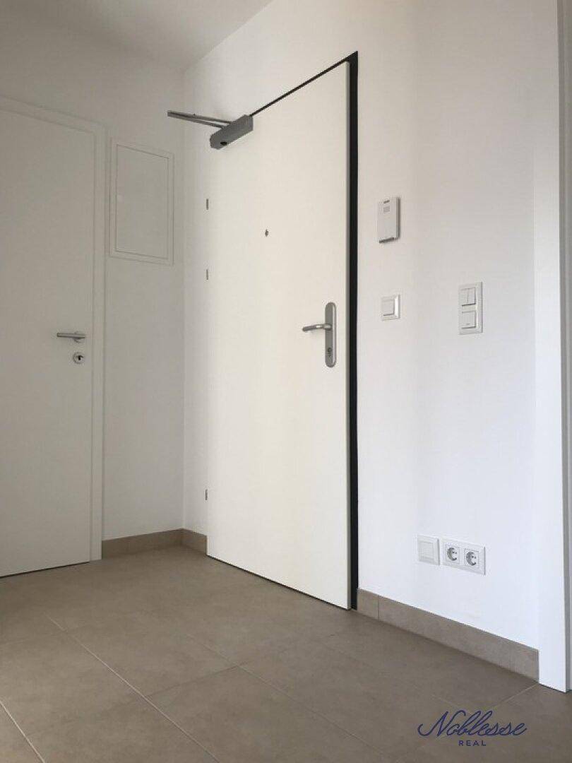 Eingangsbereich mit Sicherheitstür, hellen Fliesen und Steckdosen an der Wand.