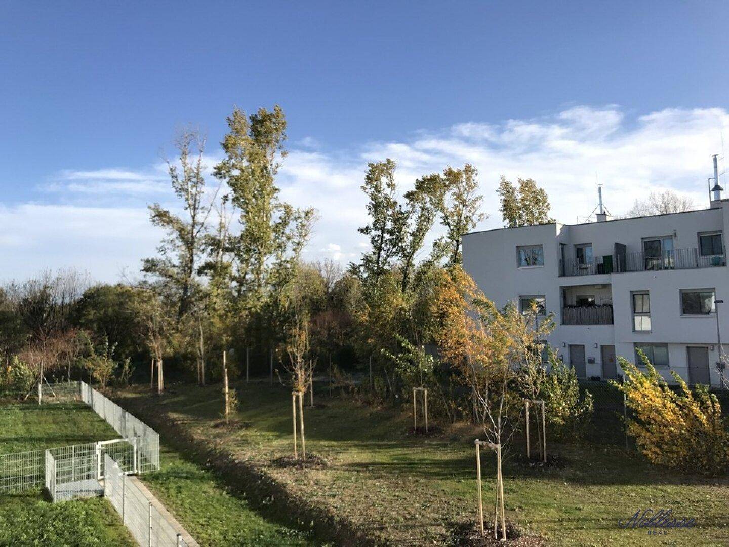 Außenansicht eines modernen Wohngebäudes mit Grünflächen und Bäumen unter blauem Himmel.