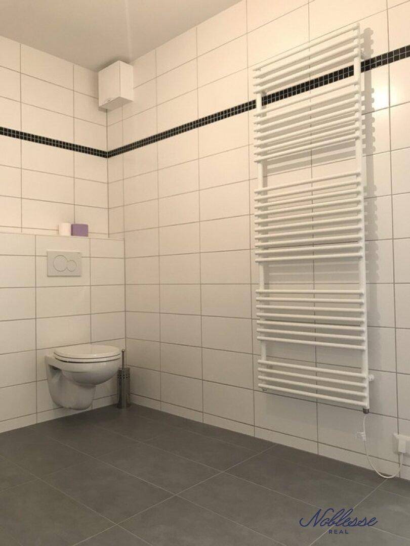 Badezimmer mit wandhängendem WC, beheiztem Handtuchhalter und weißen Fliesen.