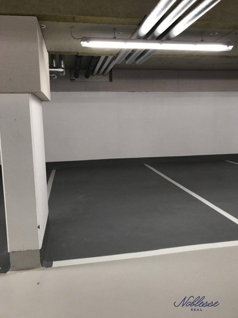 Leere Tiefgarage mit markierten Parkplätzen und Beleuchtung an der Decke.