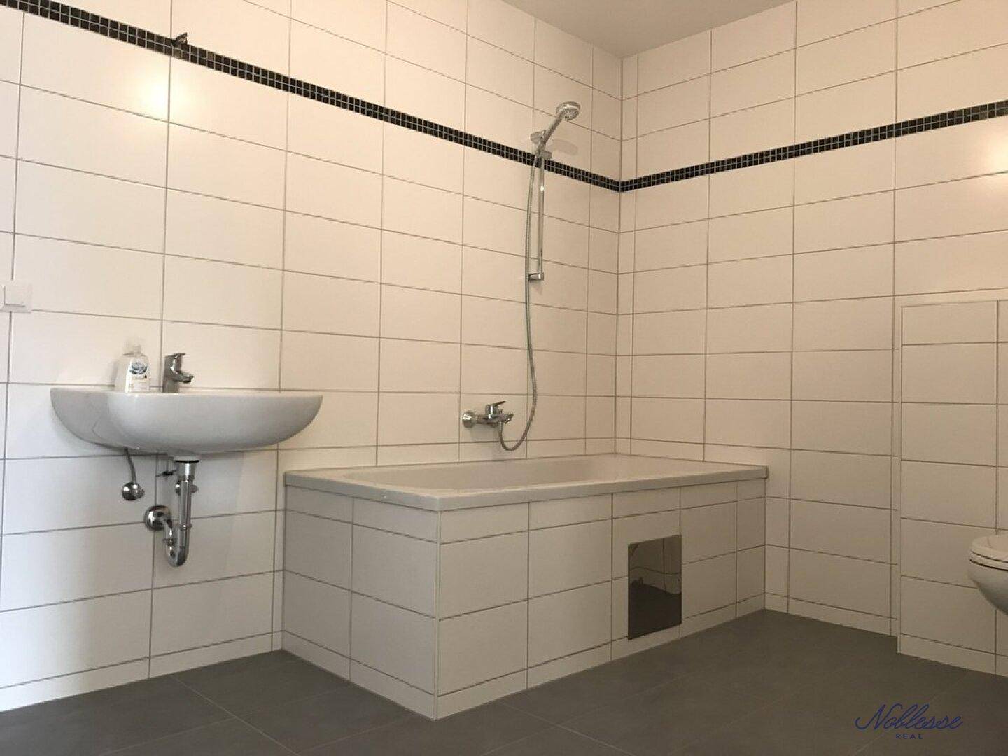 Modern gefliestes Badezimmer mit Badewanne, Duscharmatur und Waschbecken.
