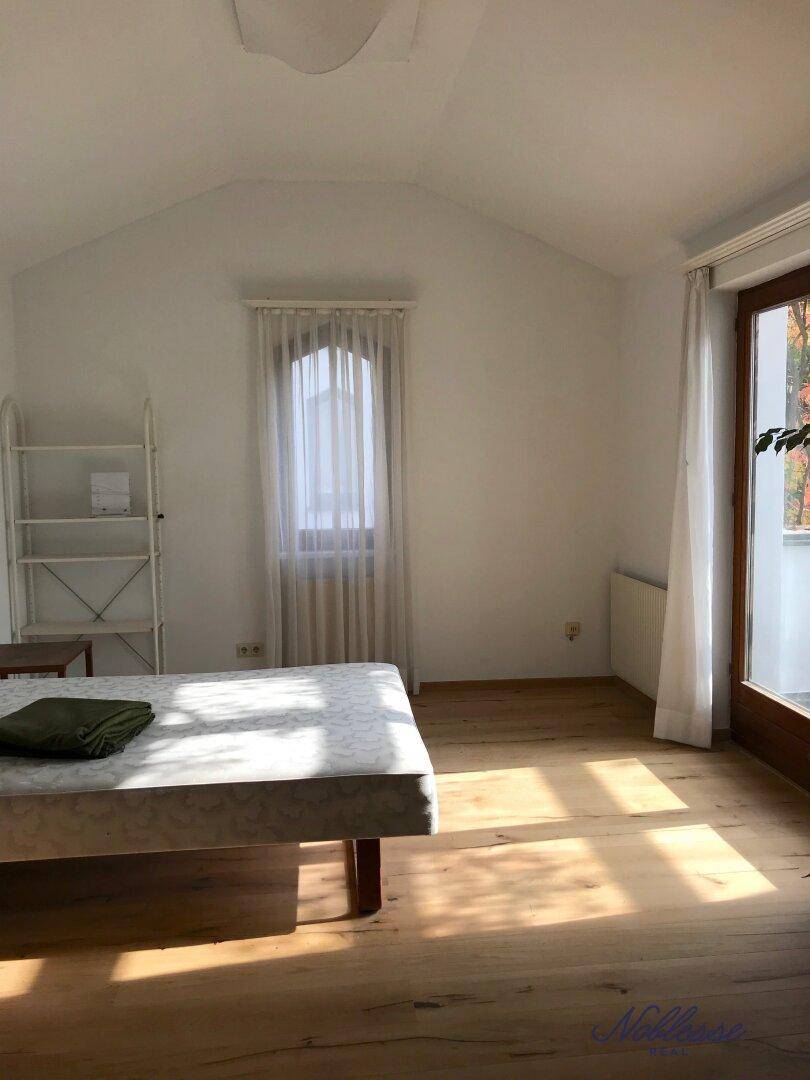 Schlafzimmer mit Holzboden, Dachschräge und Zugang zu einem Balkon.