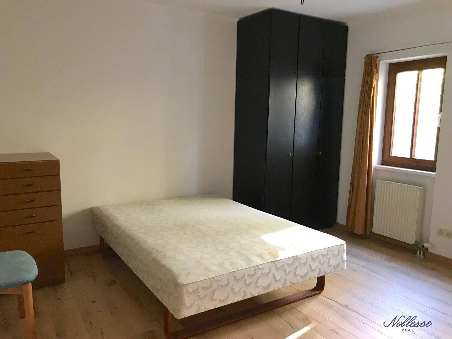 Schlafzimmer mit Holzboden, großem Kleiderschrank und Fenster für natürliches Licht.