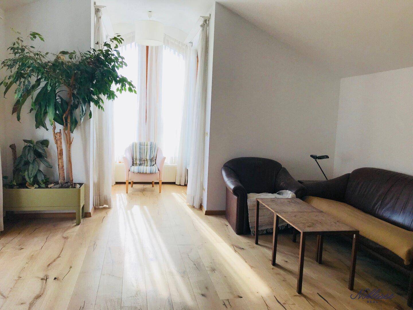 Geräumiger Wohnbereich mit Holzboden und viel Tageslicht, ideal für Entspannung.