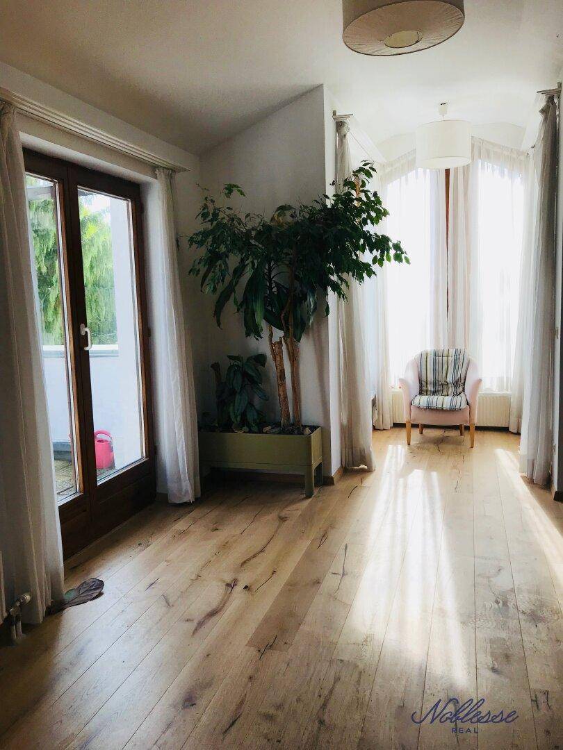 Heller Wohnbereich mit Holzboden, großen Fenstern und Zugang zu einem Balkon.