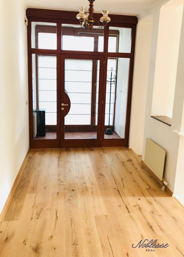 Heller Eingangsbereich mit Holzboden und großer Glastür, die viel Licht hereinlässt.