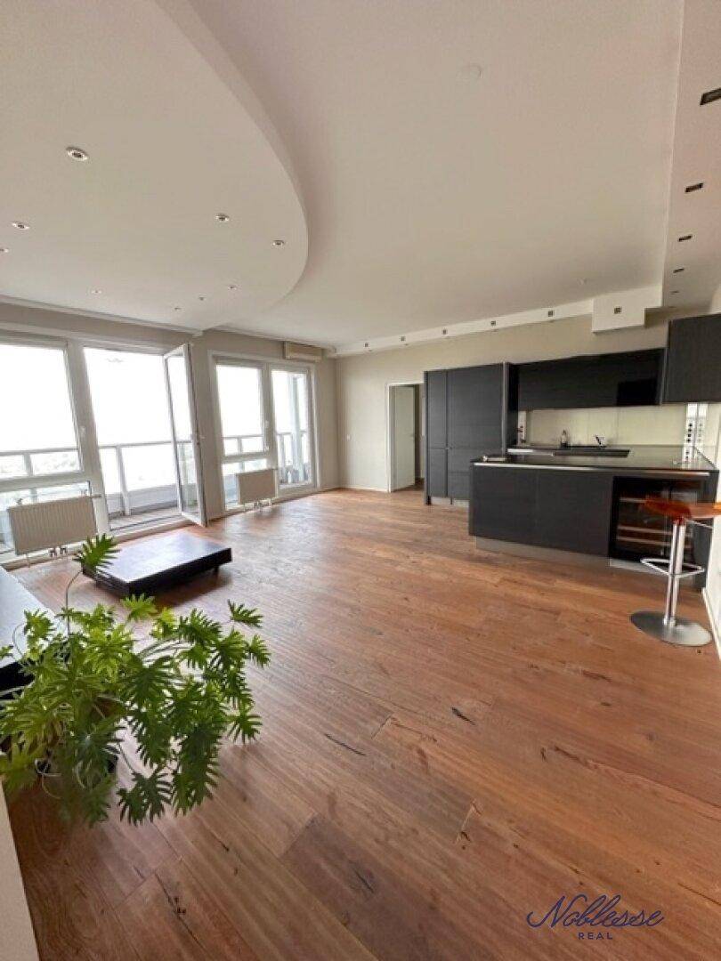 Geräumiger offener Wohnbereich mit Holzboden, integrierter Küche und Zugang zum Balkon.