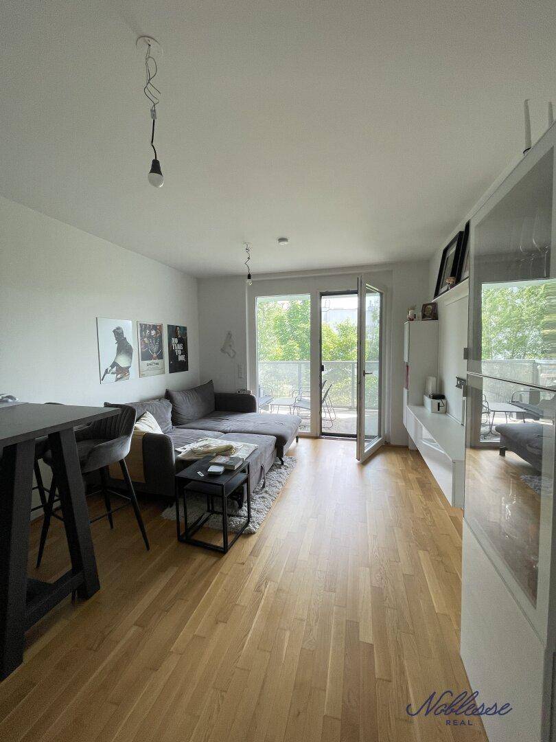 Gemütliches Wohnzimmer mit Sofa, Holzboden und Zugang zu einem Balkon mit Grünblick.