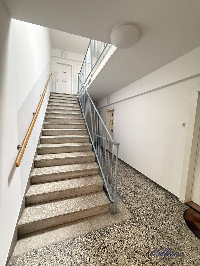 Helles Treppenhaus mit Steinstufen und Metallgeländer, führt zu den verschiedenen Etagen.