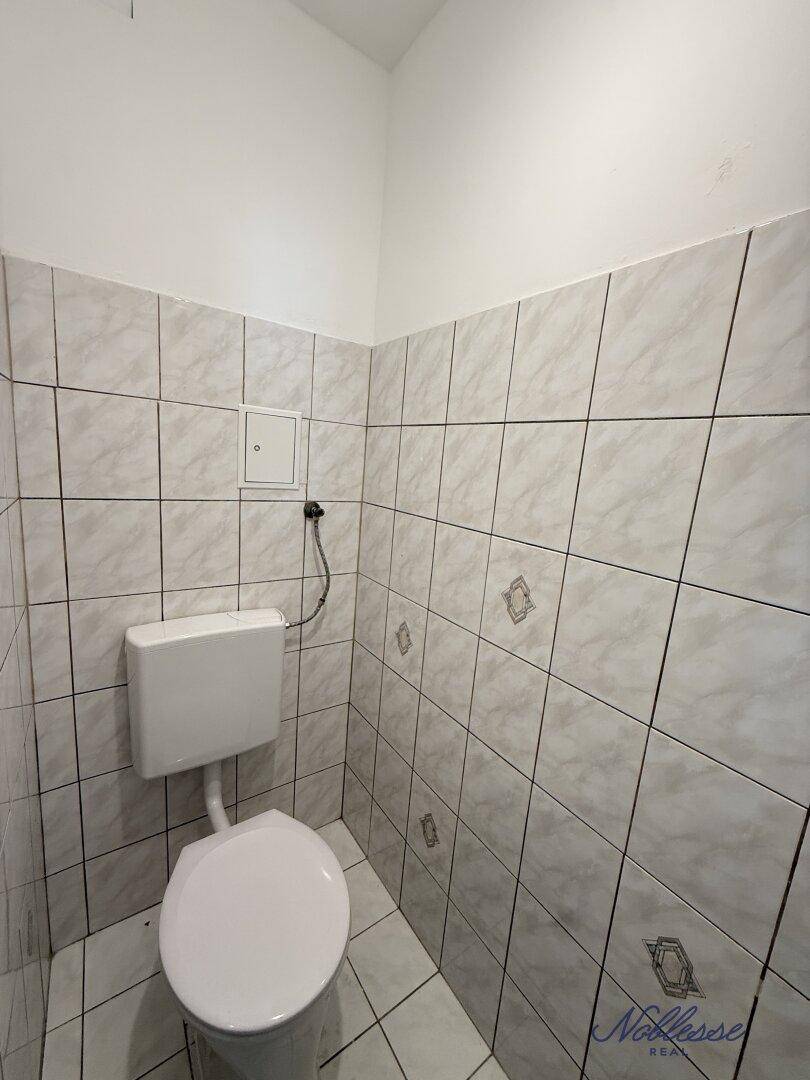 Kleines Gäste-WC mit weißer Toilette und hellgrauen Fliesen an Wänden und Boden.