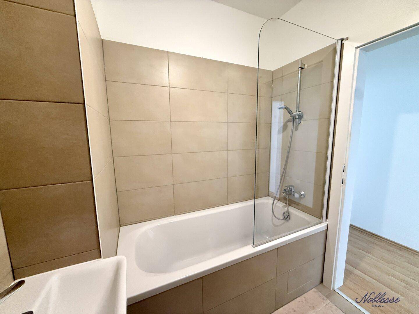 Badezimmer mit Badewanne, Duschabtrennung und beigefarbenen Fliesen, funktional und hell.