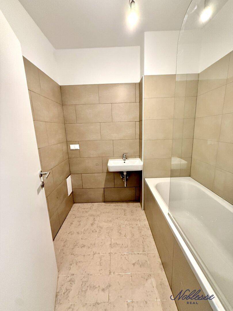 Geräumiges Badezimmer mit Badewanne, Waschbecken und beigefarbenen Wand- und Bodenfliesen.
