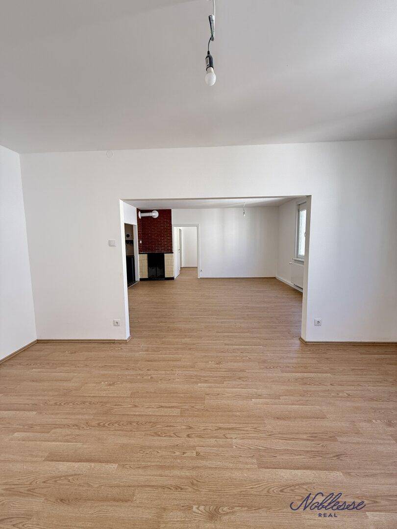 Offener Wohnbereich mit Laminatboden und Blick auf einen traditionellen Kachelofen.