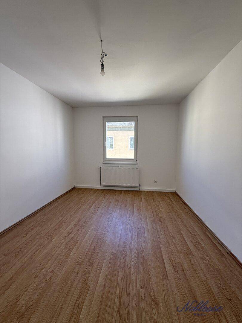 Helles, leeres Zimmer mit Laminatboden und einem Fenster, vielseitig nutzbar als Schlaf- oder Arbeitszimmer.