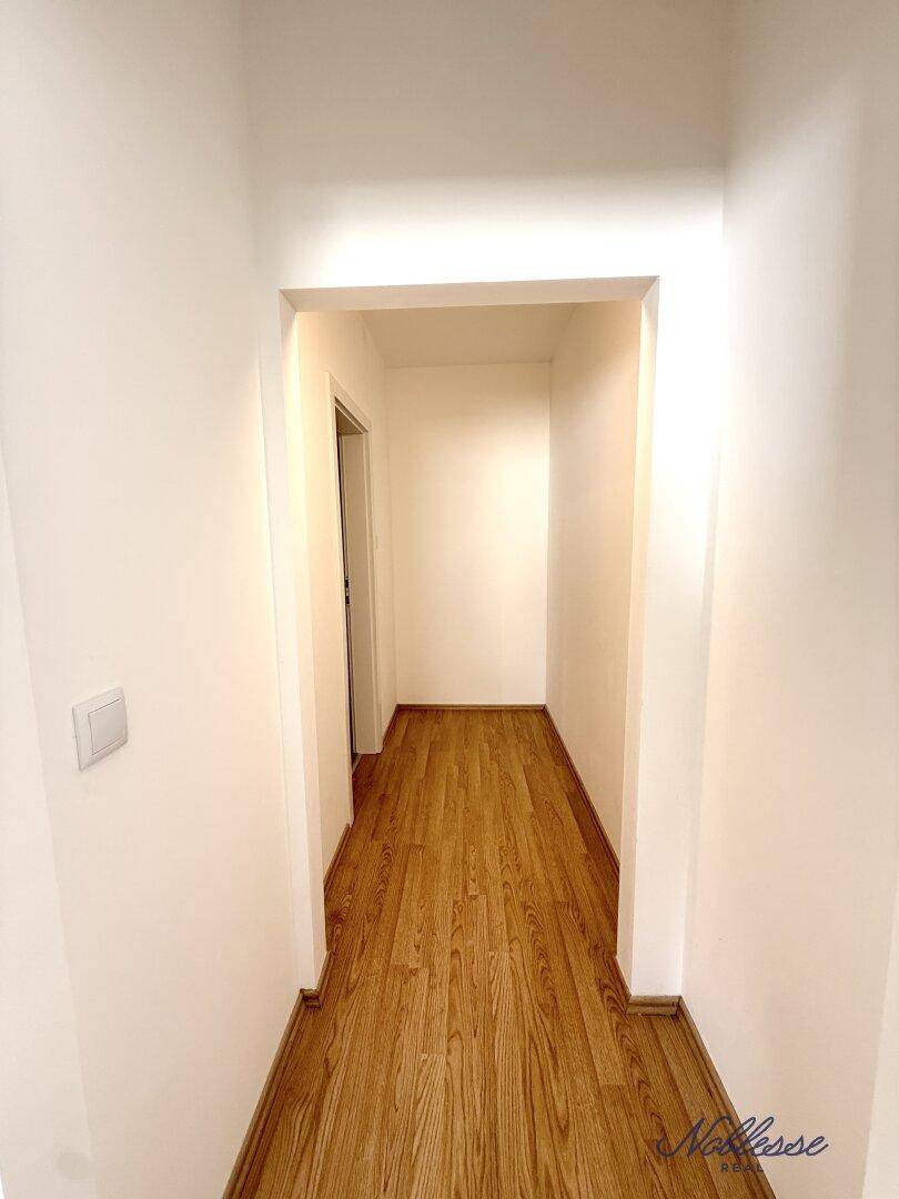 Schmaler Flur mit Laminatboden und weißen Wänden, führt zu weiteren Räumen der Wohnung.