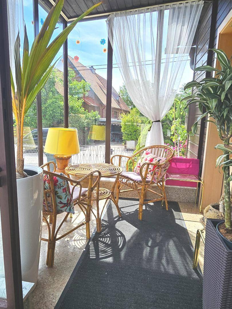 Gemütlicher Wintergarten mit Rattanmöbeln, Pflanzen und viel Tageslicht.