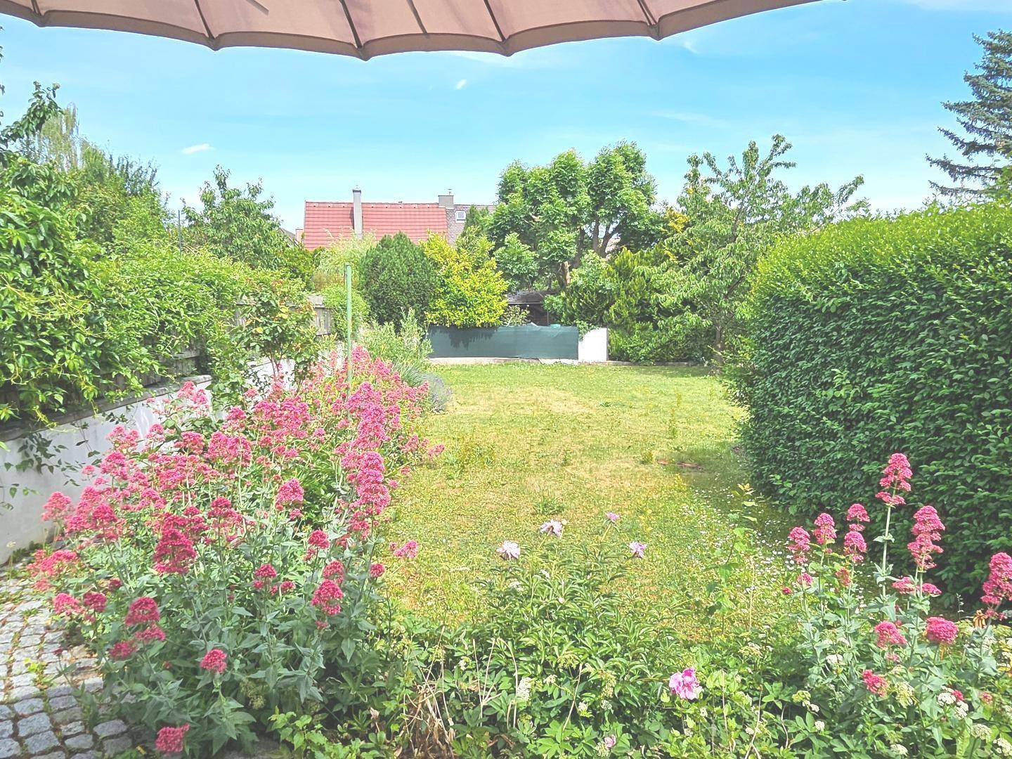 Weitläufiger Garten mit Rasenfläche, bunten Blumenbeeten und umgebenden Hecken.