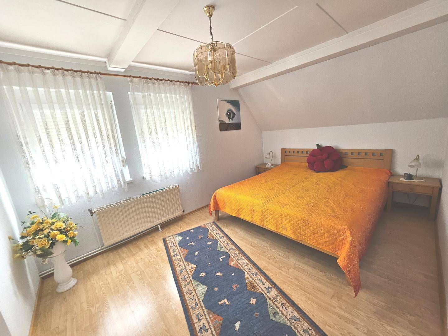 Schlafzimmer im Dachgeschoss mit Holzbalken, Laminatboden und schrägen Wänden.