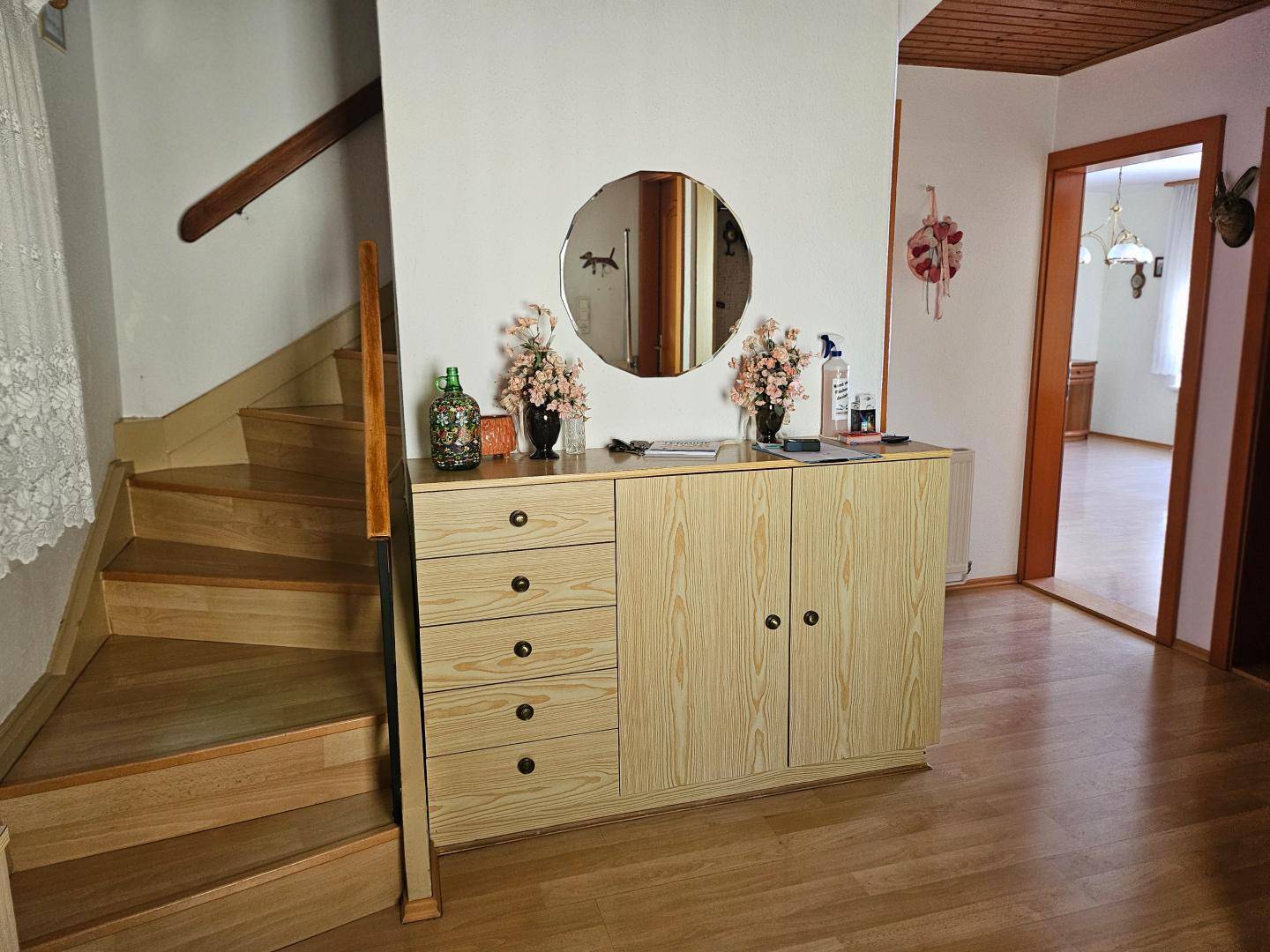 Heller Flur mit Holztreppe, Kommode und Zugang zu weiteren Räumen.