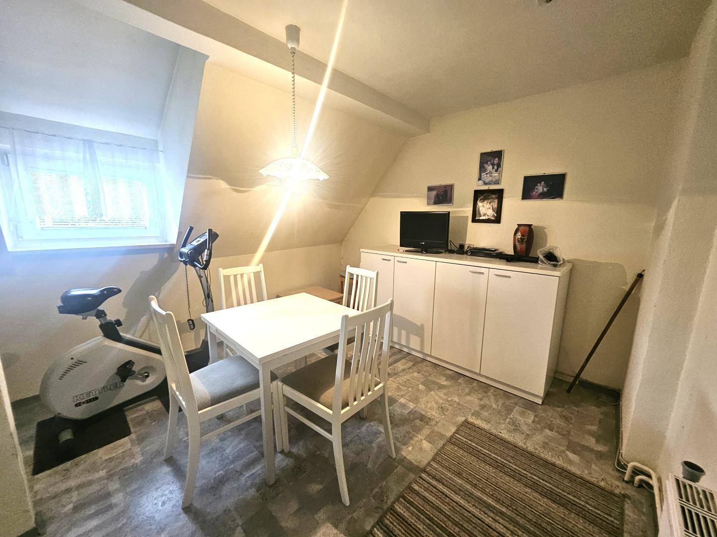 Vielseitiger Raum im Dachgeschoss mit Schreibtisch, Stühlen und Trainingsgerät.