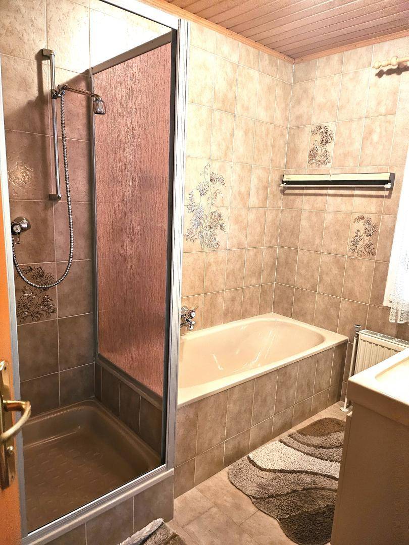 Badezimmer mit beigefarbenen Fliesen, Duschkabine und integrierter Badewanne.