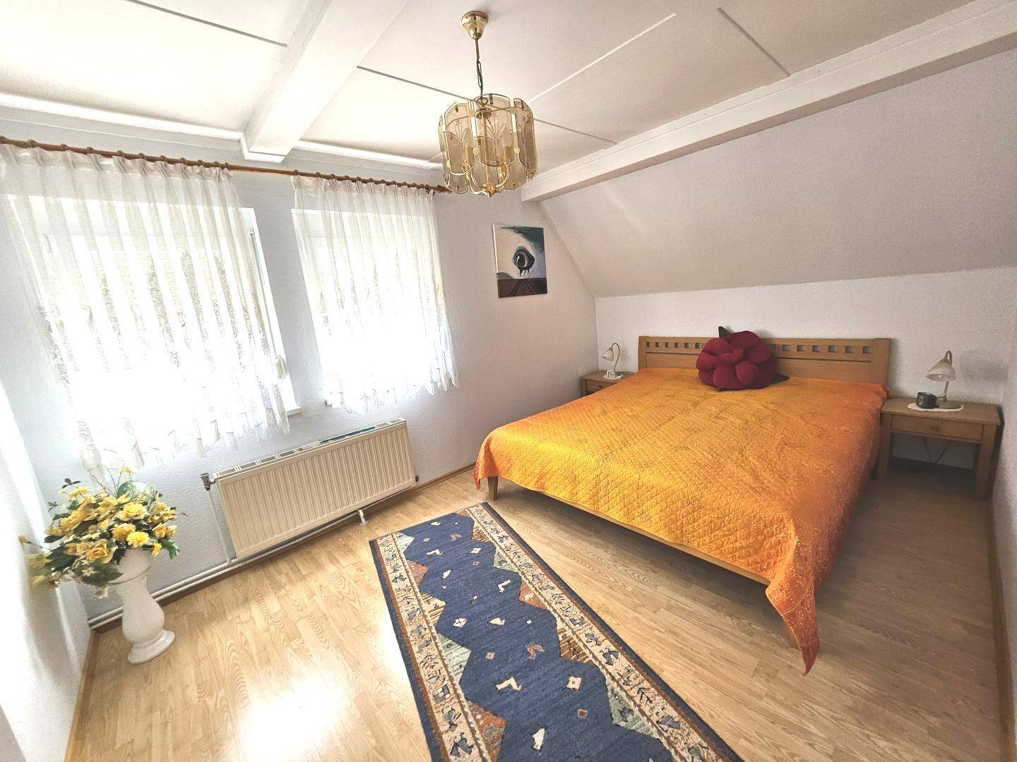 Gemütliches Schlafzimmer mit Doppelbett, Holzmöbeln und Dachschräge, hell und einladend gestaltet.