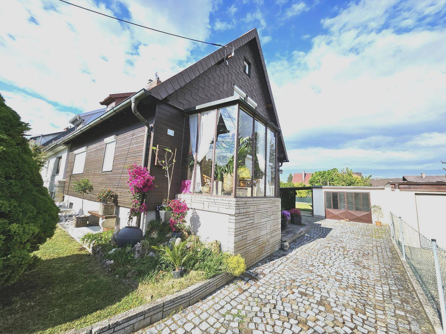 Außenansicht des Hauses mit Wintergarten, gepflasterter Auffahrt und separater Garage.
