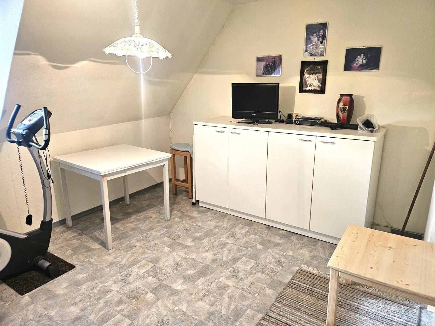 Vielseitig nutzbarer Dachbodenraum mit Schrägen, einem Tisch und einem Fitnessgerät.