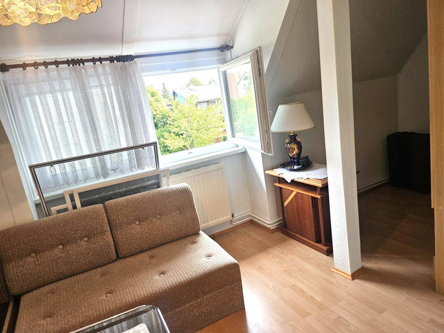 Heller Dachbodenraum mit Schrägen, einem Sofa und einem Fenster mit Blick ins Grüne.