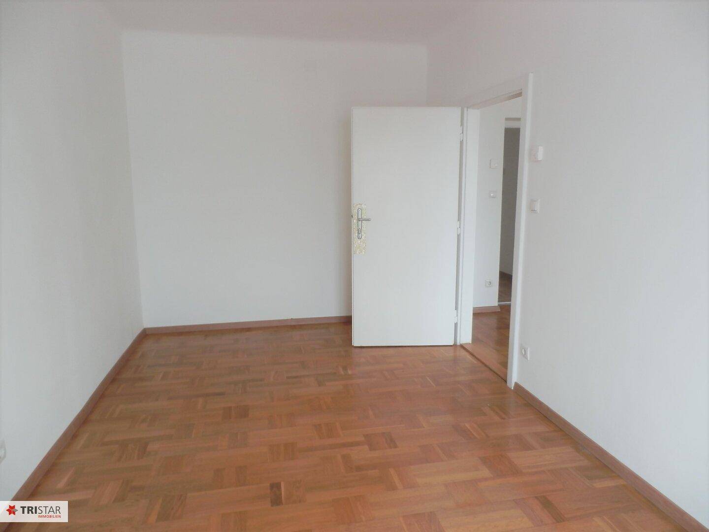 Leeres Zimmer mit Parkettboden und weißer Tür, bereit für individuelle Gestaltung.