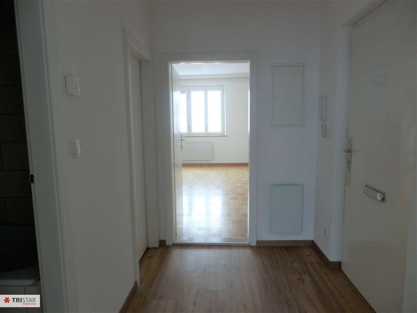 Heller Flur mit Parkettboden, der zu einem weiteren Zimmer mit Fenster führt.