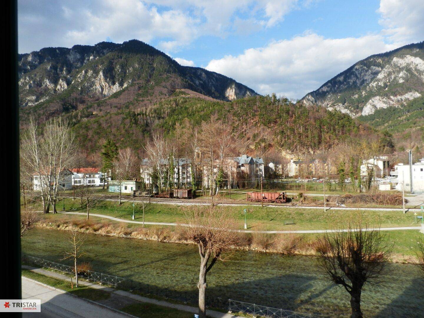 Weitläufiger Ausblick auf einen Fluss, Bäume und die beeindruckende Bergkulisse.