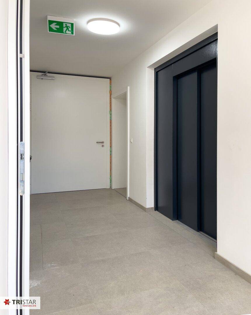 Heller Flur im Gebäude mit modernem Aufzug und Ausgangstür.