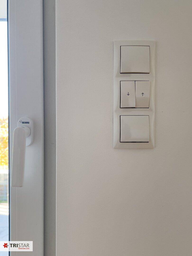 Nahaufnahme von Lichtschaltern und einem Fensterrahmen in einem hellen Innenraum.