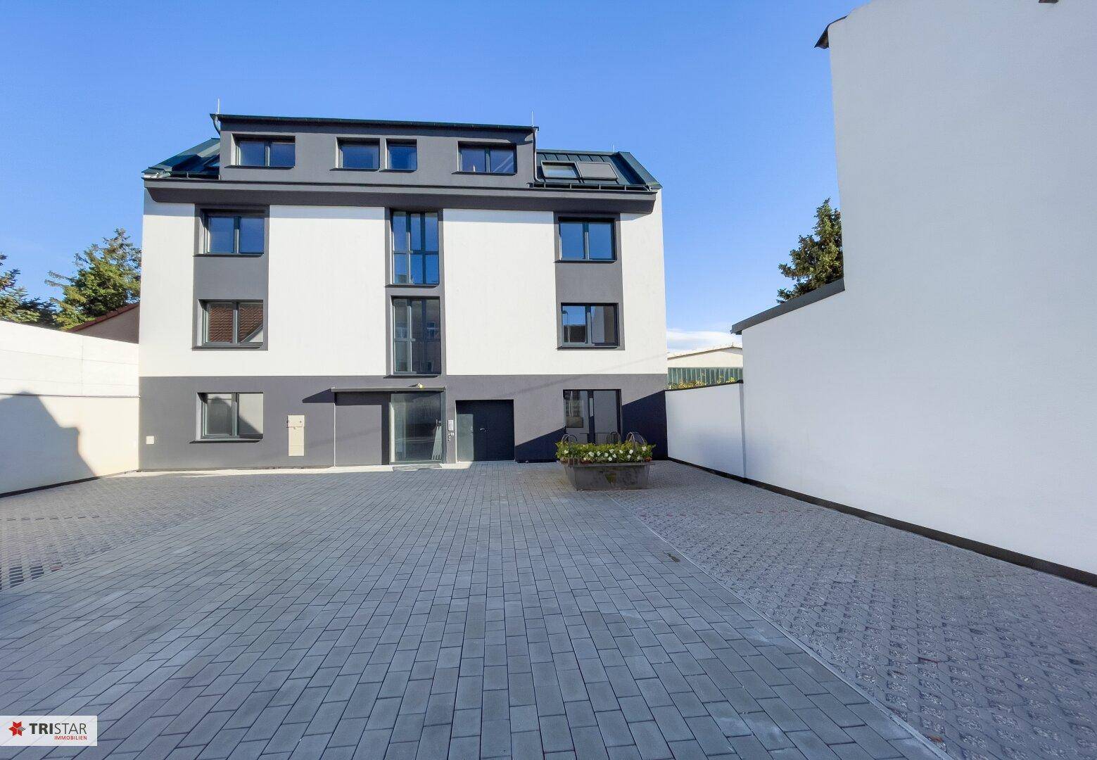 Vorderansicht eines modernen Wohngebäudes mit gepflastertem Parkplatz und klaren Linien.
